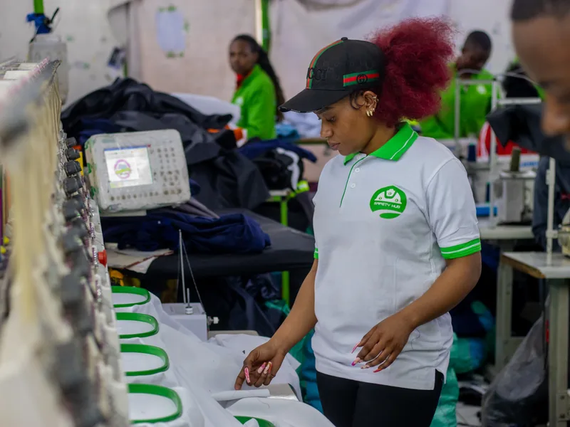 Safety Hub team member in a branded polo checking garments in the hoops of a multi-head computerized embroidery machine in the Nairobi workshop